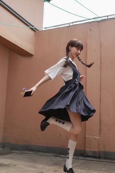 Young woman in a school uniform with braided pigtails jumping outdoors