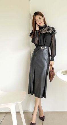 Woman in a black lace blouse and leather skirt holding a brown handbag