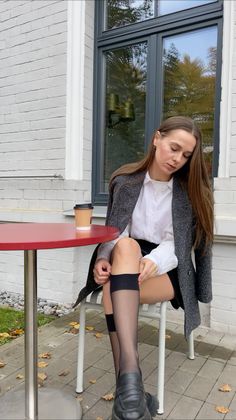 Woman in a white shirt and blazer sitting outdoors with a coffee cup