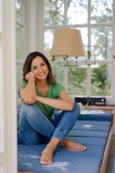 Woman in a green t-shirt and blue jeans sitting barefoot indoors