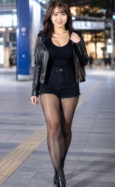 Woman in a leather jacket and black shorts walking on a street at night