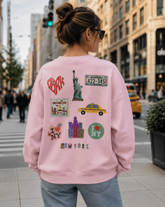 Woman in a pink sweatshirt with New York themed stickers on a city street
