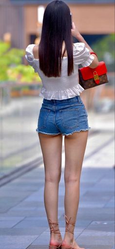 Woman in denim shorts and a white top from behind, holding a phone
