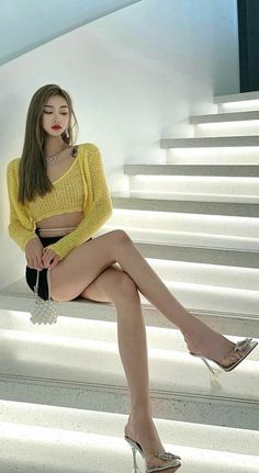 Woman in a yellow crop top and black shorts sitting on illuminated stairs
