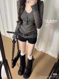 Person in a gray long-sleeve top, black shorts, and platform boots with a cross necklace