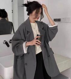 Woman in an oversized blazer with a messy bun holding a cup indoors