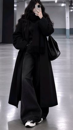 Person in a long black coat and wide leg jeans taking a mirror selfie