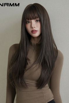 Woman with long brown hair and bangs wearing a brown long-sleeved top indoors