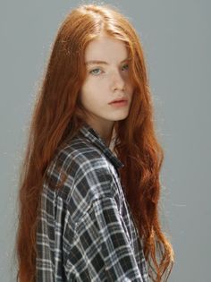 Woman with long red hair and blue eyes wearing a plaid shirt