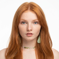 Woman with red hair and freckles wearing feather earrings and a beaded necklace