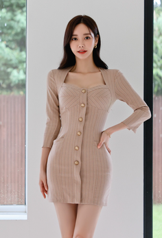 Woman in a beige dress with gold buttons posing indoors