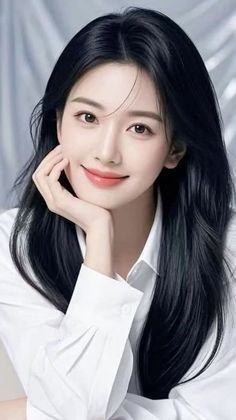 Woman with long black hair wearing a white shirt, smiling and resting her chin on her hand