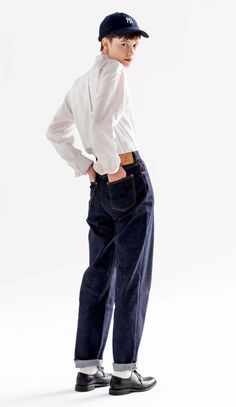 Person in a baseball cap, white shirt, and dark jeans with hands in pockets