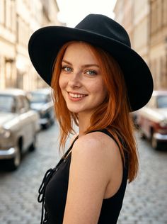 Woman with red hair and freckles wearing a black hat and top on a cobblestone street