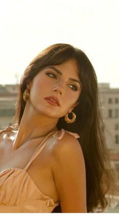 Woman with long dark hair and gold earrings in a peach dress outdoors