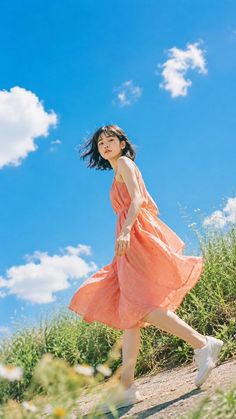 Woman in a peach dress walking outdoors under a bright blue sky