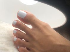 Foot with white pedicure under a bright lamp on a white furry surface