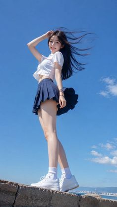Woman in a white crop top and blue pleated skirt posing outdoors under a blue sky