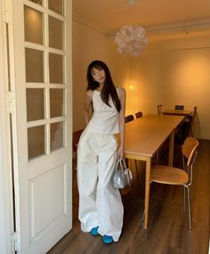 Woman in a white top and wide leg pants with blue shoes and a silver bag indoors