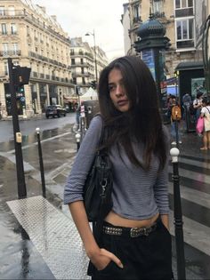 Woman with long dark hair wearing a striped shirt and studded belt on a city street