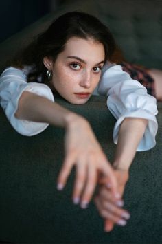 Woman with freckles and dark hair wearing a white shirt, looking directly at the camera