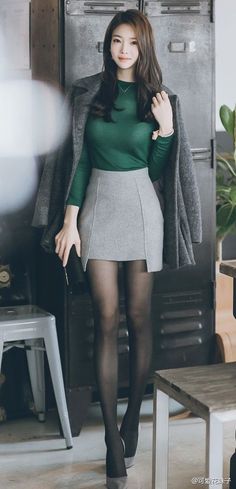 Woman in a green top and grey skirt with black pantyhose and high heels