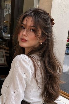 Woman with long brown hair and a white embroidered blouse looking over her shoulder