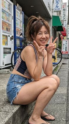 Woman in denim shorts and a tank top squatting on a street