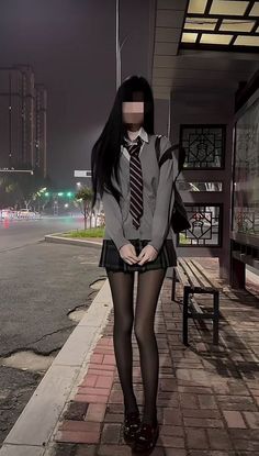Person in a school uniform with long black hair standing at a bus stop at night