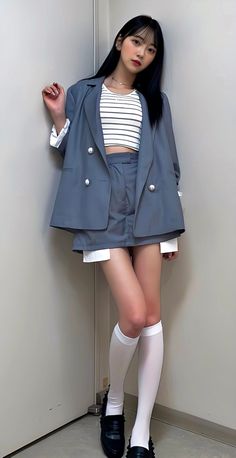 Woman with long black hair wearing a suit jacket, shorts, and crop top indoors