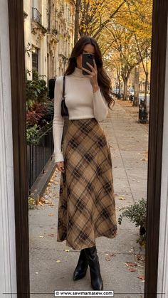 Woman in a plaid skirt and turtleneck sweater taking a mirror selfie outdoors