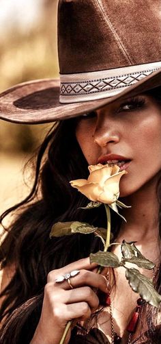 Woman in a cowboy hat holding a yellow rose to her lips