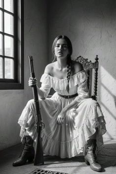 Woman in an off-shoulder dress and boots holding a long rifle, sitting indoors