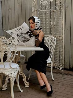 Woman in a black dress and polka dot scarf reading a newspaper at an outdoor cafe