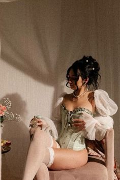 Woman in a light green corset and white stockings holding a perfume bottle
