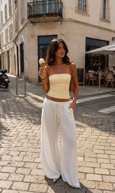 Woman in a strapless top and wide leg pants holding an ice cream on a cobblestone street