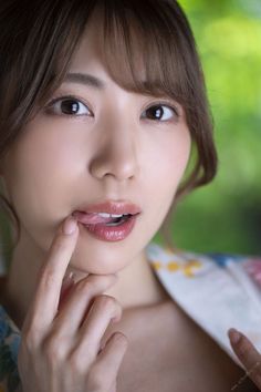 Woman with brown hair and bangs, finger on her lips, with a green background