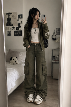 Woman in a hoodie and cargo pants taking a mirror selfie in a bedroom