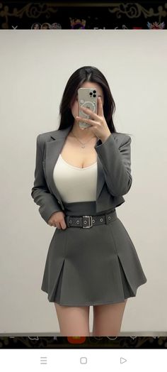 Woman in a gray blazer and pleated skirt taking a mirror selfie