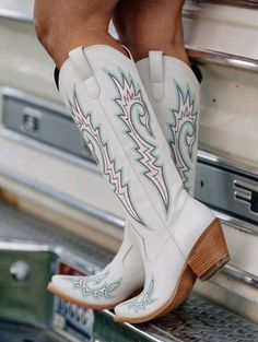 White cowboy boots with blue and purple embroidery on a metal surface