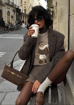 Woman in a blazer and plaid shorts drinking coffee on a city street
