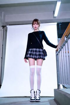 Woman in a black sweater and plaid skirt with white thigh highs in a studio