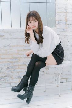 Woman with long hair wearing a white shirt and black shorts, sitting on a white chair