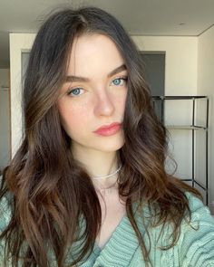 Woman with long brown hair and blue eyes wearing a green sweater indoors