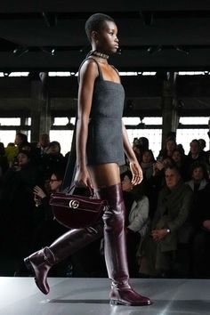 Model walking the runway in a dark mini dress and thigh-high boots