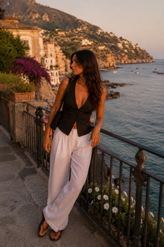 Woman in a black vest and white pants on a coastal balcony at golden hour