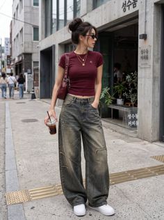 Woman in a crop top and baggy jeans with a messy bun and sunglasses on a street