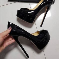 A hand holding a black patent leather platform high heel shoe