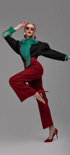 Woman in red pants, black top with green bow, and red sunglasses posing