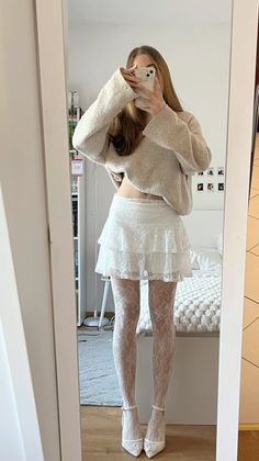 Woman in a white lace skirt and cropped sweater taking a mirror selfie